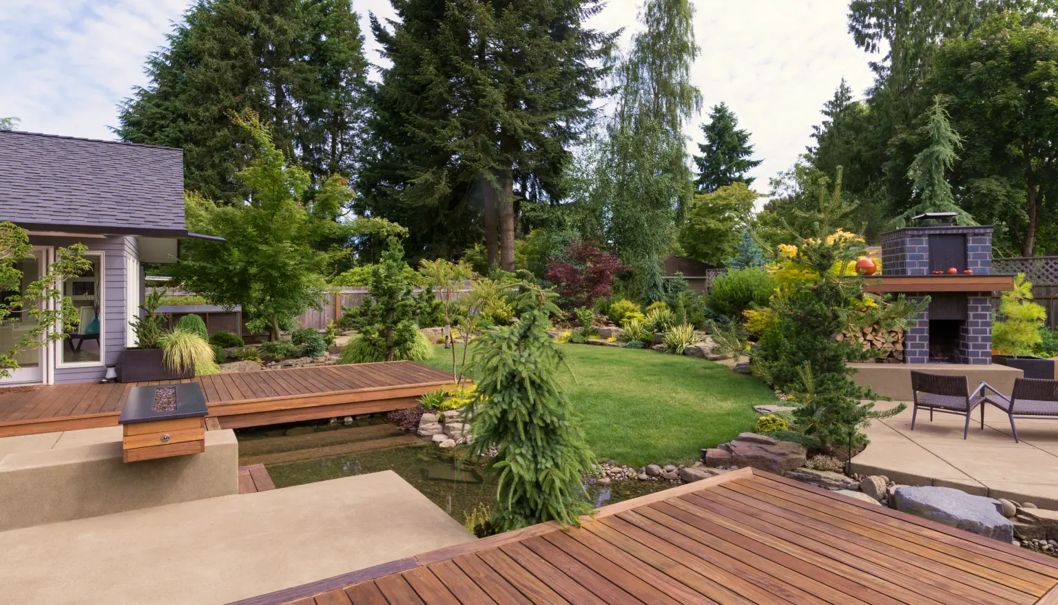 Photo of a beautiful landscaped garden with a small river, field of grass and decking with furniture, for Soper Landscapes