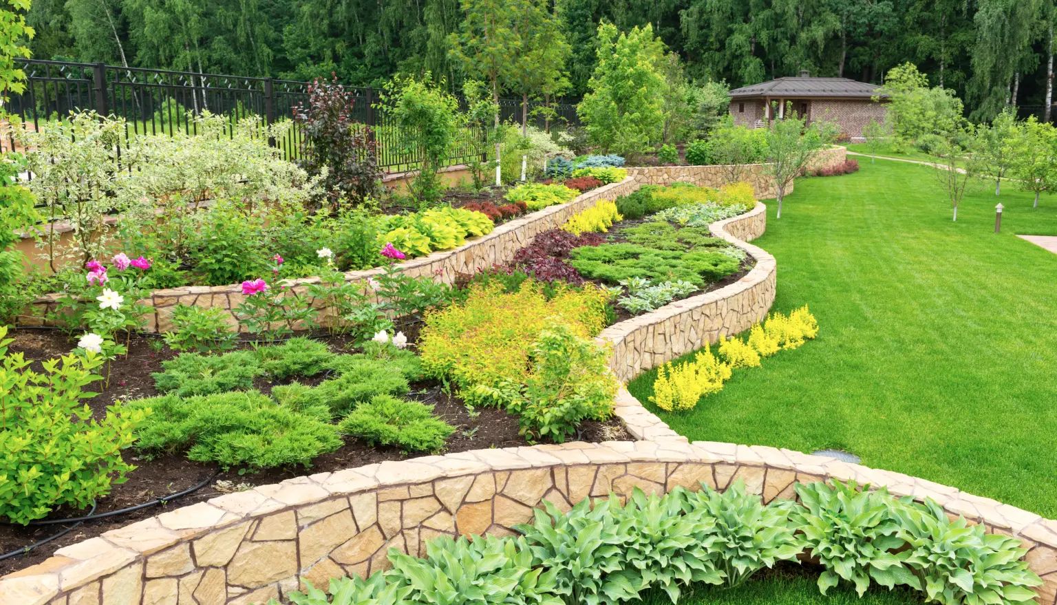 Photo of house garden with brick walled patches of elevated flowers and green grass