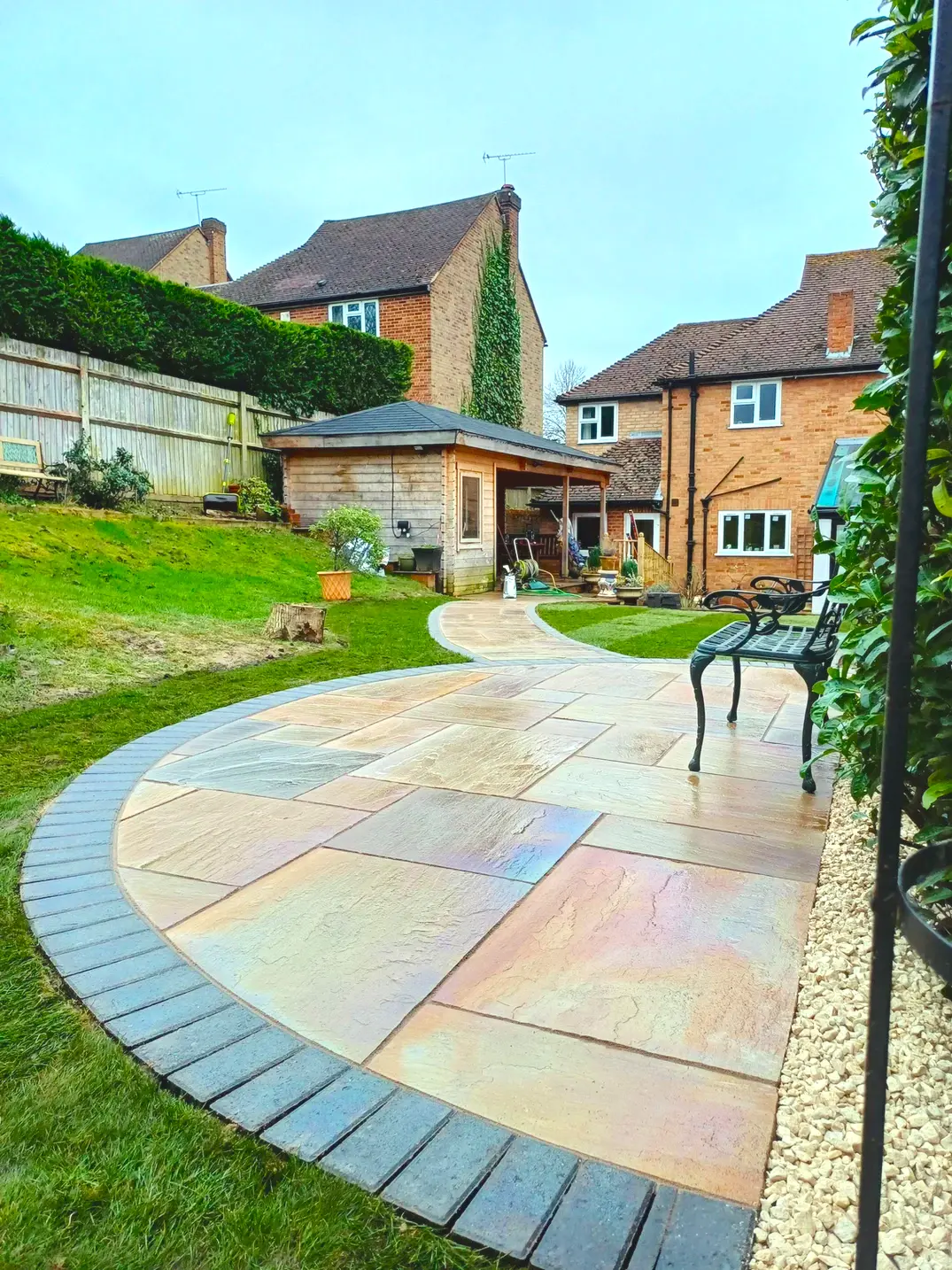 Photo of a garden with green grass and stone patio and pathway with a house on the background